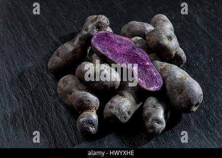 Intero e fette di patate viola sull'ardesia Foto Stock