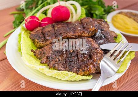 Bistecca di carne di maiale, grigliate con anelli di cipolla e verdure fresche, erbe aromatiche Foto Stock