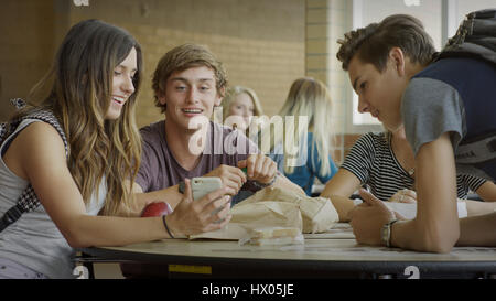 Gli studenti di mangiare il pranzo e utilizzando il telefono cellulare durante la rientranza nella mensa scolastica Foto Stock