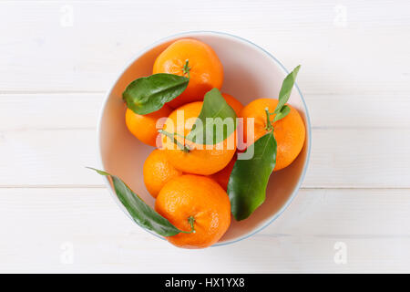 Ciotola di mandarini freschi con foglie su sfondo bianco Foto Stock