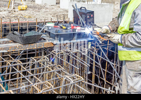 Colpo industriali di costruzione lavoratore che è la saldatura telaio metallico, della gabbia di armatura all'interno del legno smontabile stampo per la cementificazione pilastro di base. Foto Stock