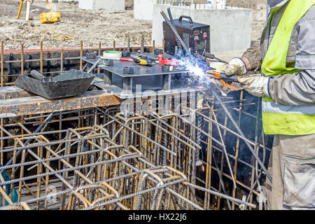 Colpo industriali di costruzione lavoratore che è la saldatura telaio metallico, della gabbia di armatura all'interno del legno smontabile stampo per la cementificazione pilastro di base. Foto Stock