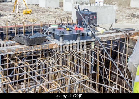 Colpo industriali di costruzione lavoratore che è la saldatura telaio metallico, della gabbia di armatura all'interno del legno smontabile stampo per la cementificazione pilastro di base. Foto Stock