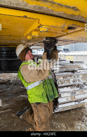 Mt. Clemens, Michigan - un lavoratore per Homrich, una demolizione contraente, prepara attrezzature pesanti per il trasporto presso il sito di un garage per il parcheggio demoliti Foto Stock