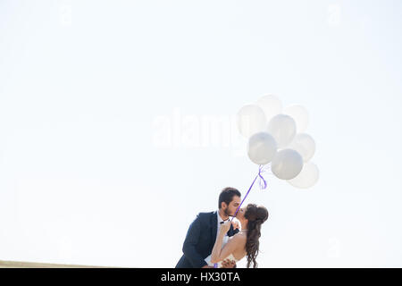 Proprio felice coppia sposata con palloncini in mano sul cielo bianco Foto Stock