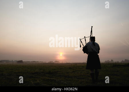 Un musicista suona la cornamusa nei campi al tramonto. Foto Stock