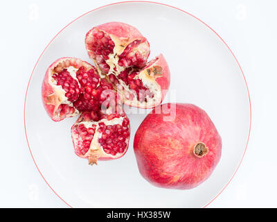 Due maturi frutti di melograno e suddiviso in quattro parti, su un bianco piastra di porcellana. La piastra con un confine di melograno. Foto Stock