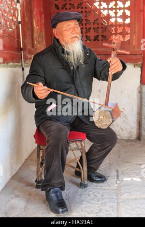 ShiGu, Cina - 17 Marzo 2017: il vecchio cieco uomo cinese la riproduzione di antichi cinesi strumento a corda nel villaggio di ShiGu. Foto Stock