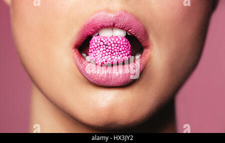 Di un bel colore rosa le labbra con un pezzo di dolce candy. Close up della giovane donna con la caramella in bocca.