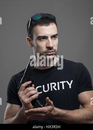 Fiducioso toccare macho guardia di sicurezza il ricarico gun guardando lontano. Contrasty atmosferica ritratto su grigio di sfondo per studio. Foto Stock