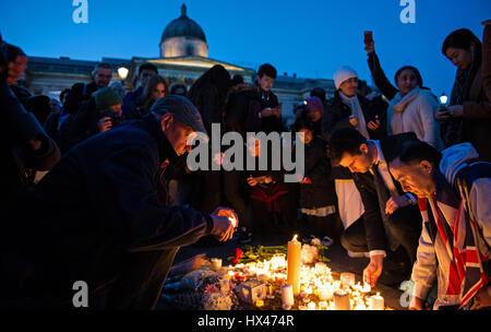 Un uomo in un tappo piatto tra gli altri accende una candela in una veglia a Trafalgar square in memoria di tutte le vittime e onore di tutti coloro che sono stati colpiti dal terrore di Westminster attentato in cui un funzionario di polizia e numerosi turisti e membri del pubblico dove ucciso il 22.3.17 Foto Stock