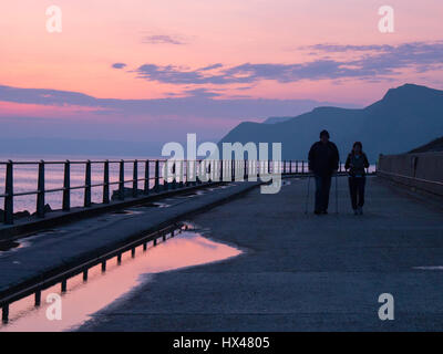 Westbay, Dorset, Regno Unito. Il 24 marzo 2017. Due persone a piedi lungomare come il cloud infine si cancella e un vago ma colorato tramonto segue. Con un meteo alto insieme a seguire e temperature più calde previsto per questo fine settimana. © Dan Tucker/Alamy Live News Foto Stock