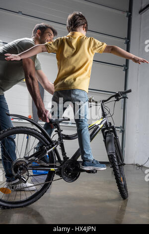 Padre holding bicicletta con carino piccolo figlio di piedi su di esso Foto Stock