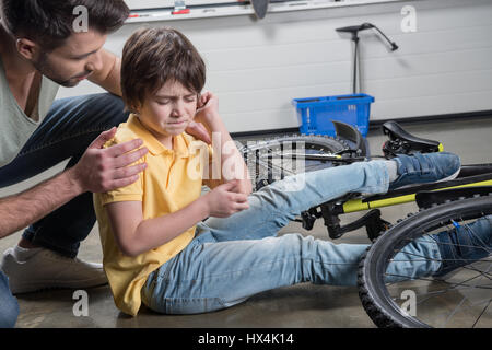 Padre aiutando feriti figlio di alzarsi dal cadere da noleggio Foto Stock