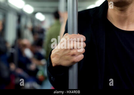 Primo piano di un giovane uomo caucasico del viaggio come un passeggero in una carrozza del treno, in piedi e afferrando una barra verticale con la sua mano destra Foto Stock