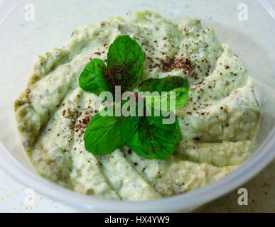 Una pentola di Arabo libanese mutabal dip o baba ganoush,realizzato da tahini e melanzane arrosto, guarnita con un rametto di menta e una spolverata di sommacco Foto Stock