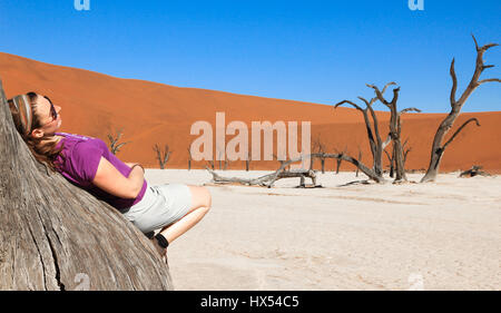 La donna si appoggia su albero nel deserto circondato. godendo e rilassante. Foto Stock