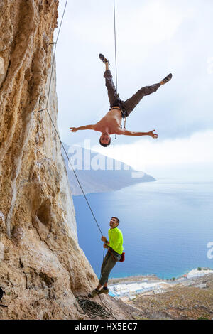 Arrampicatori ingannare intorno: un uomo appeso a testa in giù mentre viene abbassato, belayer guardando lui e sorridente Foto Stock