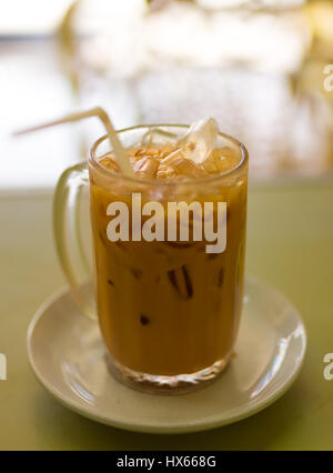 Un bicchiere di vetro di iced Thai tè con cubetti di ghiaccio e una paglia su un piattino impostato in un ristorante. Foto Stock