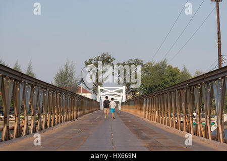 Il dorso di due bambini a piedi attraverso un metallo fiume attraversando ponte in Cambogia. Foto Stock