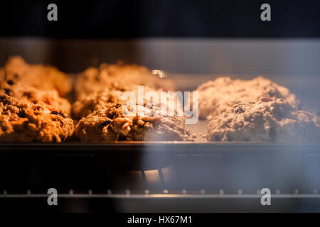 Torte fresche e cottura in aumento in un forno domestico. Il tiro viene effettuato attraverso la porta del forno di vetro e illuminata dalla luce del forno Foto Stock