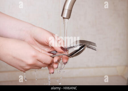 Le mani di un close-up girl. ragazza lava forchette e cucchiai sotto flusso di acqua Foto Stock