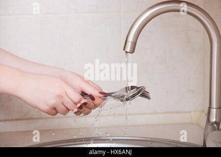 Le mani di un close-up girl. ragazza lava forchette e cucchiai sotto flusso di acqua Foto Stock