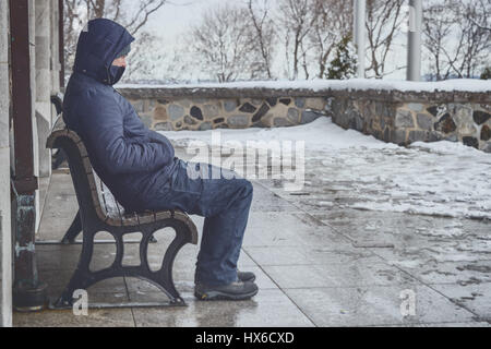 Uomo seduto su un banco in inverno con neve sul terreno Foto Stock