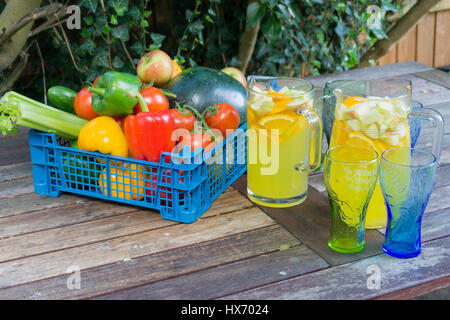 Visualizzazione di frutta e verdura con una brocca di succo di arancia e bicchieri su un tavolo esterno in un giardino Foto Stock
