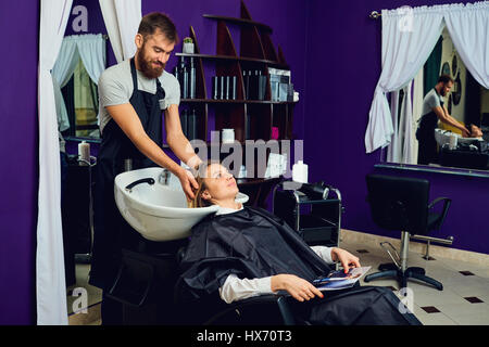 Un parrucchiere uomo lava i capelli in testa al cliente in sedia b Foto Stock