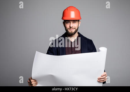 Ritratto di un architetto builder studiando piano di disposizione delle camere, serio ingegnere civile che lavora con i documenti sul sito in costruzione. Foto Stock