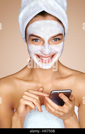 Donna con maschera facciale tramite telefono cellulare. Foto di attraente giovane donna ricevere trattamenti spa. Beauty & Skin care concept Foto Stock