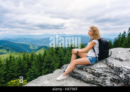 Una giovane donna si erge sulla cima di una montagna in nuvoloso meteo godendo della vista Foto Stock