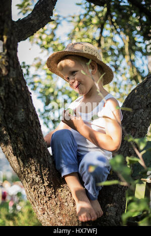 Ritratto all'aperto: bellissimo piccolo ragazzo seduto su un albero e l'azienda Apple Foto Stock