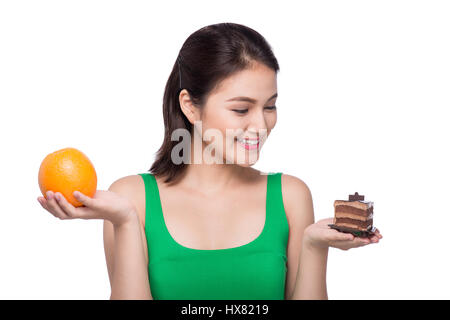 La dieta. Concetto di dieta. Cibo sano. Bella giovane donna asiatica scegliendo tra frutta e dolci Foto Stock