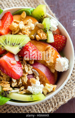 Macedonia di frutta fresca con muesli fatti in casa, il formaggio feta e miele sulla piastra bianca per una sana dieta vegana vegetariana colazione biologica, cibo, pasto, insalata Foto Stock