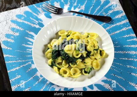 Le cime di rapa collard (verdi) di pasta (Italiano Orecchiette alle cime di rapa) servita in un piatto bianco con forcella su bianco e azzurro placemat Foto Stock