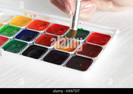 Processo di pittura con acquarelli, una tavolozza e pennello in mano Foto Stock
