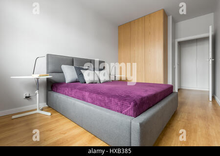 Camera da letto progettato in stile minimalista con grande letto grigio e alta armadio in legno Foto Stock