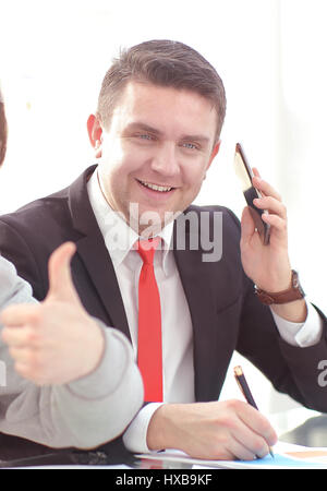 Inquadratura di un bel giovane imprenditore in un elegante e moderno spazio per uffici con grandi finestre, parlando al telefono e guardando al di fuori Foto Stock