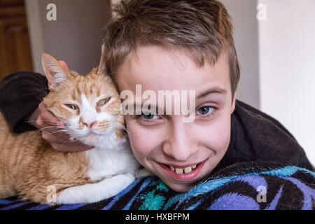 Quattordici anni di vecchio ragazzo scherzosamente abbracciando e spremitura di Kia, il suo breve domestici di pelo di gatto Foto Stock