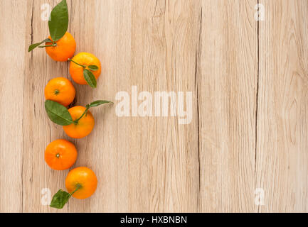 La disposizione delle clementine fresche con foglie in legno marrone chiaro con sfondo spazio copia su entrambi i lati. Foto Stock