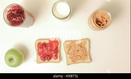 La prima colazione con un panino con marmellata e burro di arachidi, un bicchiere di latte e un apple. Vaso con marmellata e burro di arachidi sul tavolo Foto Stock