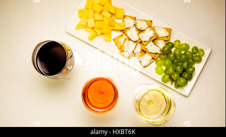 Tre bicchieri riempiti con rosso, bianco e rosato con uno snack su un piatto da portata, formaggio, uva pane con formaggio morbido Foto Stock