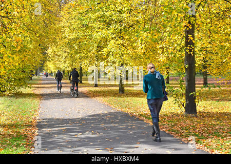 I giardini di Kensington Londra Inghilterra Foglie di autunno pedone walker & noleggio bici ciclista in anticipo sulla condivisione consentita percorso ciclo percorso in Royal Park Foto Stock