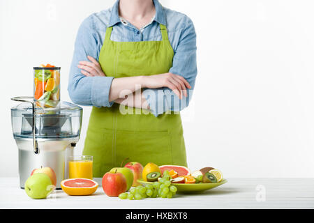 Anonimo donna che indossa un grembiule, la preparazione di succhi di frutta freschi utilizzando moderne spremiagrumi elettrico, uno stile di vita sano concetto su sfondo bianco Foto Stock