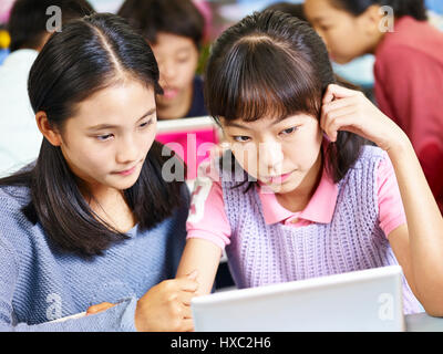 Due asian scuola elementare ragazze guardando il computer tablet pensando duro mentre si lavora in gruppi. Foto Stock