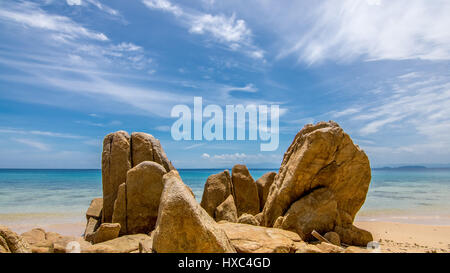 Ampia spiaggia di sabbia dorata di rocce di pietra su un isola tropicale spiaggia guardando fuori per un tranquillo paradiso mare. Foto Stock