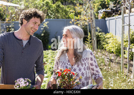 Felice coppia portando vasi di fiori, giardinaggio nel giardino soleggiato Foto Stock