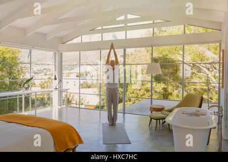 Uomo maturo la pratica dello yoga con le mani incrociate in testa nella camera da letto di lusso Foto Stock